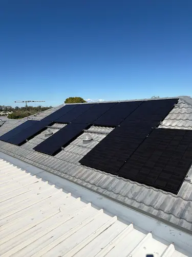 Black solar panels installed on a residential tiled roof under a clear blue sky